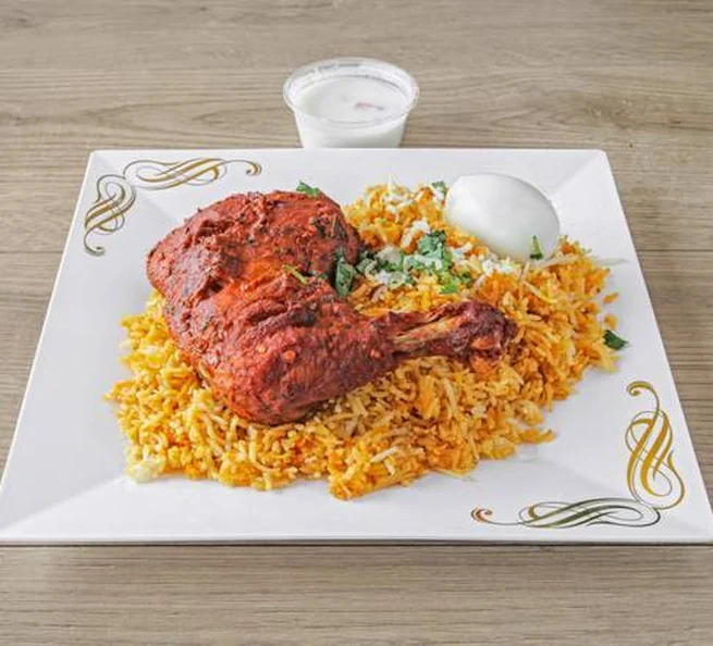 Chicken biryani with a fried chicken leg, boiled egg and raita