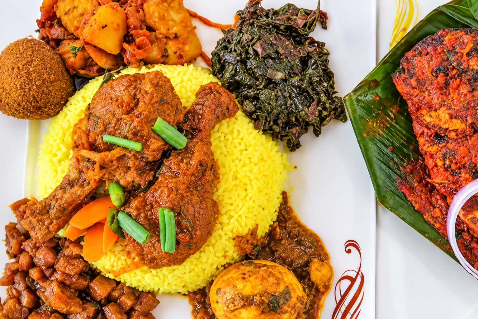Yellow rice with chicken curry, boiled egg curry, potato curry, sautéed greens and a fish cutlet, with masala-grilled fish on banana leaf